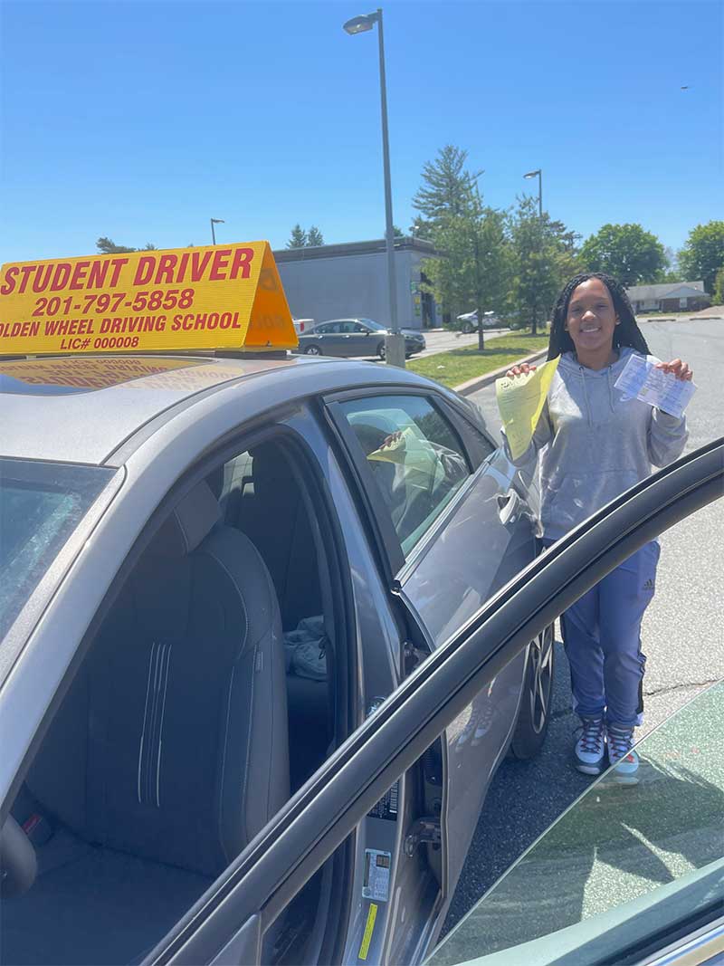 Golden Wheel student holding a passed road test beside the school car.